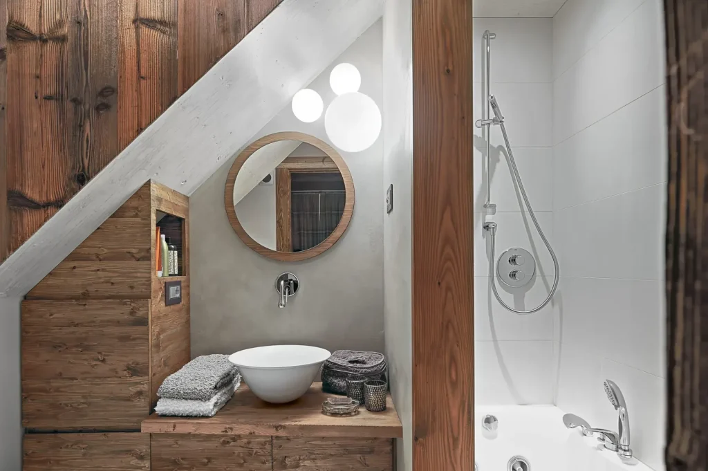 rustic bathroom interior, in the  foreground the counter top washbasin on the wooden washbasin  cabinet and the round mirror, on the right there is the  bathtub